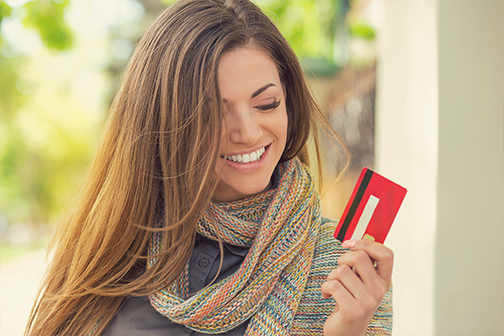 Cheerful excited young woman with credit card standing outdoors